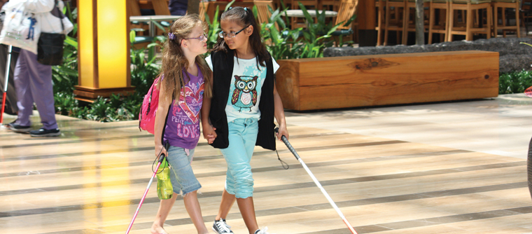 Two young girls walk together with their long white canes